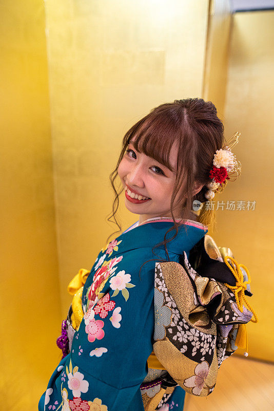 在“Seijin Shiki”成年仪式上，身着Furisode和服的年轻女子在金色的“Byobu”折叠屏风前向后看的肖像